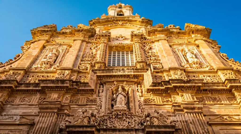 Close up of the intricate Lecce Baroque carvings on the golden carparo limestone facade of Sant'Agata Cathedral in Gallipoli.